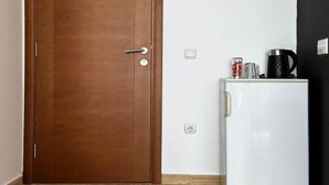 A closed wooden door with a handle and a white refrigerator with a black coffee maker and a glass on top. - Casa Mila Apartments - Studio apartment with sea view (Ulcinj)