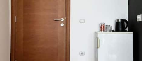 Una puerta de madera cerrada con manija y un refrigerador blanco con una cafetera negra y un vaso encima.