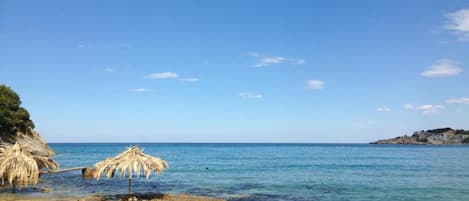 A beach with clear water, a thatched umbrella, and rocky terrain.