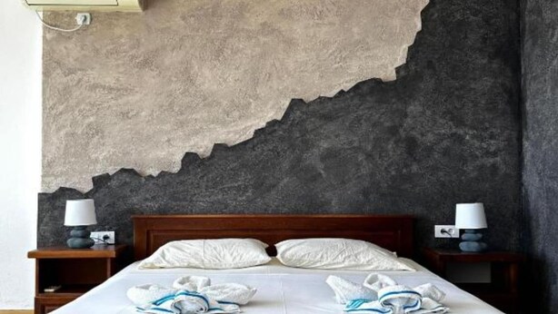 A hotel room with a large bed, two bedside tables with lamps, and a wall with a textured surface. - Casa Mila Apartments - Studio apartment with sea view (Ulcinj)