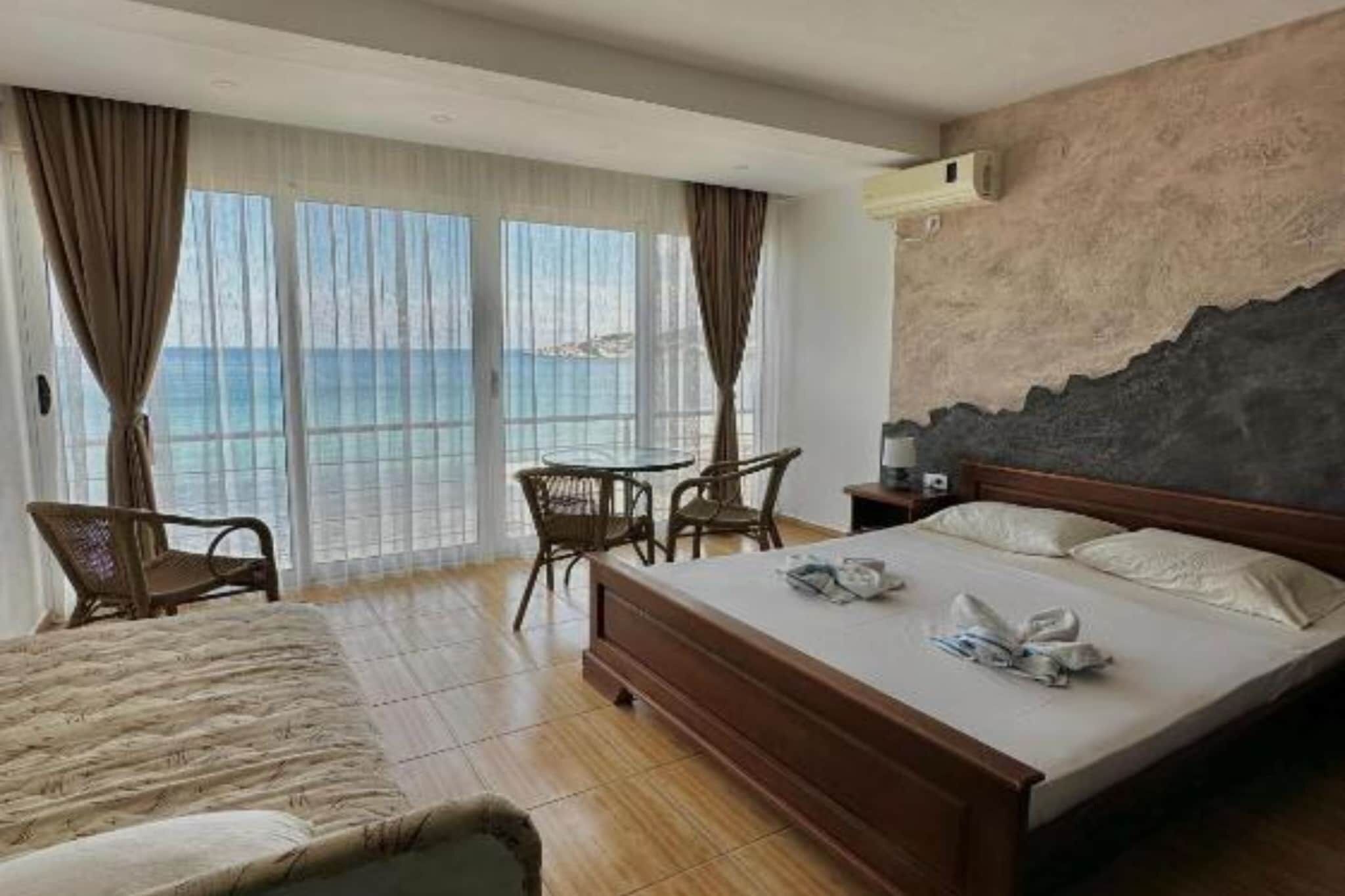 Habitación de hotel con cama, escritorio, dos sillas, vista al mar y un ventanal con cortinas.