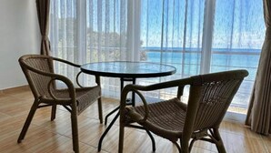A room with a round table and two wicker chairs, large windows with curtains, and a view of the sea. - Casa Mila Apartments - Studio apartment with sea view (Ulcinj)
