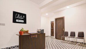 Un mostrador de recepción con un cartel que indica que es atendido por OYO, un área de recepción con sillas, una planta en maceta y un suelo estampado.