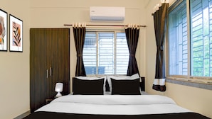Habitación de hotel con cama, mesita de noche, aire acondicionado y ventana con cortinas.