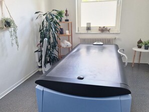 Ein Zimmer mit einem langen, dunkelbraunen Tisch, einem Heizkörper, einem Fenster mit Jalousien und einem kleinen Tisch mit einer Pflanze.