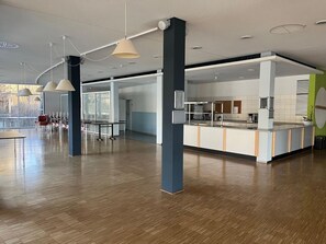 Ein geräumiger Innenbereich mit einer langen Theke, mehreren Pendelleuchten und Blick durch große Fenster.