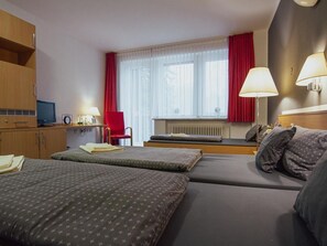 Ein Hotelzimmer mit zwei Betten, einem Schreibtisch, einem Stuhl, einem Fernseher und einem Fenster mit Vorhängen.