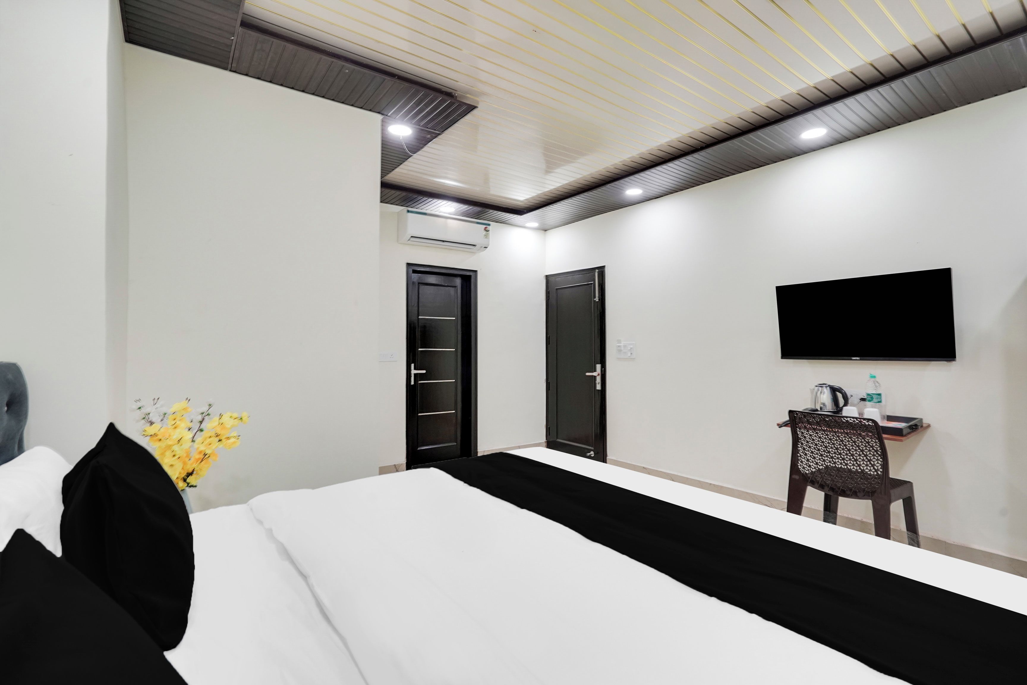 Una habitación de hotel con cama, televisor de pantalla plana, escritorio con silla y equipo de aire acondicionado.