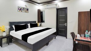 A hotel room with a bed, a desk, a chair, a door, and a wall-mounted air conditioner. - Super Collection O Nirman Vihar (New Delhi)