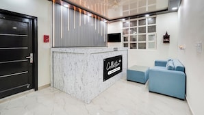 A reception area with a marble counter, a black door, a blue sofa, and a window with blinds. - Super Collection O Nirman Vihar (New Delhi)