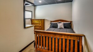 A bedroom with a wooden bed, a dresser, a mirror, and a ceiling with recessed lighting.
