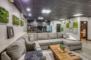 Una sala de estar moderna con un sofá modular, una mesa de centro de madera y una cocina al fondo.