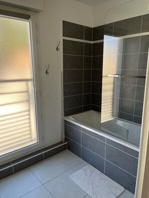 Ein Badezimmer mit Badewanne, dunklen Fliesen, einem Fenster mit Milchglas und einer Duschkabine.