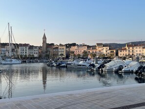 A marina with boats docked, a prominent church tower, and residential buildings in the background. - Charming 2-bedroom apartment with parking near port in Sanary-sur-Mer (Sanary-sur-Mer)