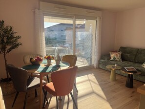 A living room with a dining area, a green sofa, and a view through a sliding glass door. - Charming 2-bedroom apartment with parking near port in Sanary-sur-Mer (Sanary-sur-Mer)