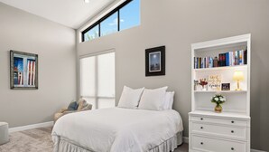 Un dormitorio con una cama grande, un aparador blanco, una estantería y una ventana con vistas al cielo.