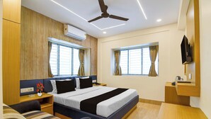 A hotel room with a bed, bedside tables, a desk, a ceiling fan, and windows with curtains. - Super Collection O Newtown Bus Stand (Barasat)