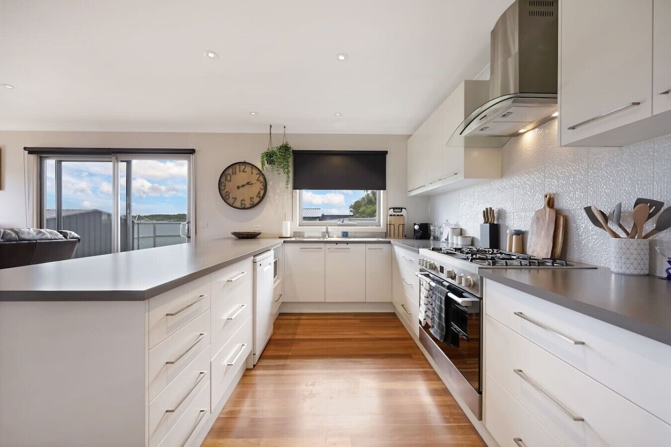 A modern kitchen with white cabinetry, a wooden floor, a built-in oven, and a large window.