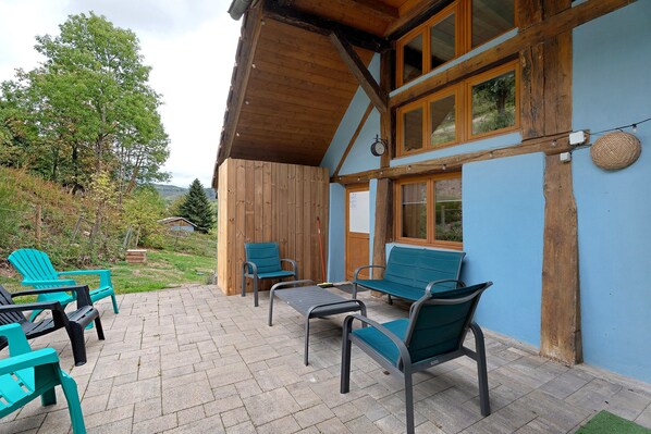 A wooden house with a patio area featuring outdoor seating and a view of the surrounding landscape.