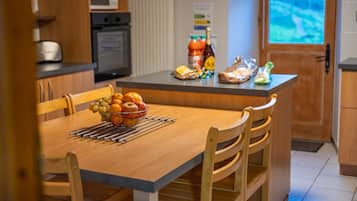 Una cocina con una mesa de comedor, sillas, un frutero, un microondas, un refrigerador y una ventana con vistas.