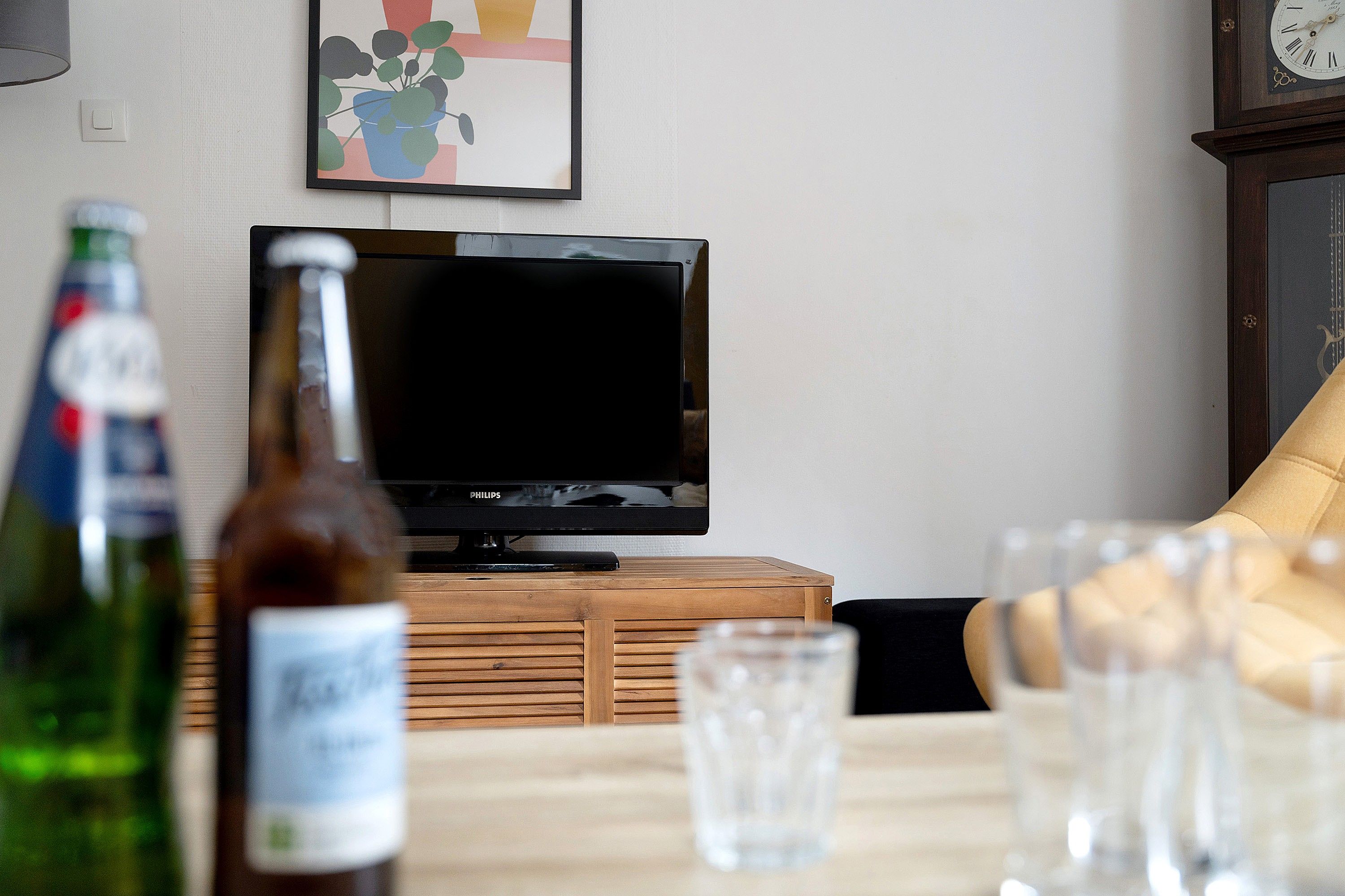 Ein Wohnzimmer mit Fernseher auf einem Holzständer, einer Bierflasche und einem Glas auf einem Tisch.