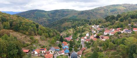 A hillside village with traditional houses, a winding road, and a backdrop of forested hills.