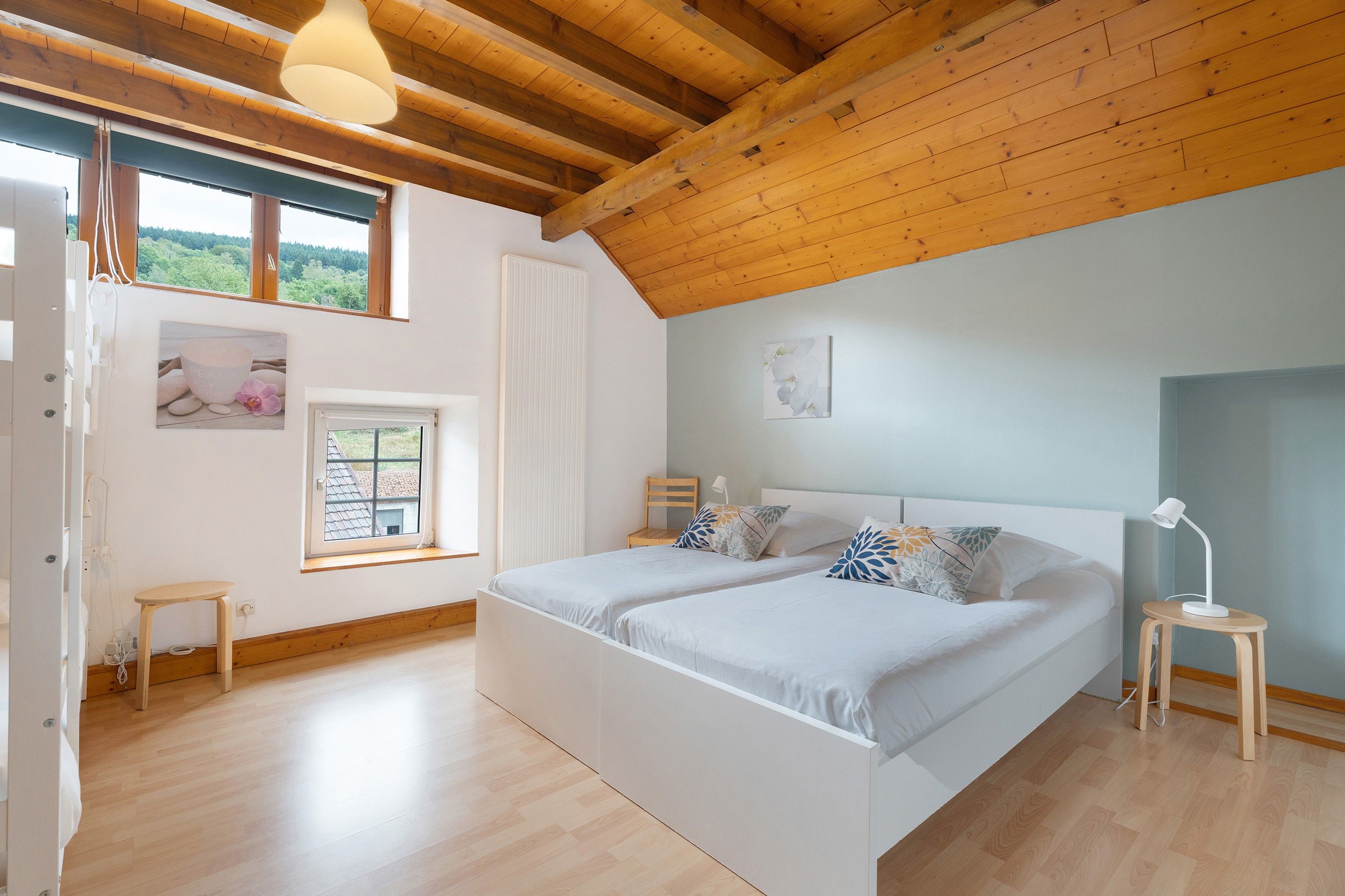Une chambre avec un plafond en bois, deux lits, une fenêtre et une table de chevet avec une lampe.
