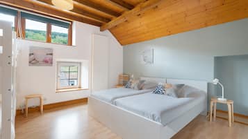 Un dormitorio con techo de madera, dos camas, una ventana y una mesita de noche con lámpara.