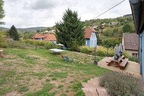 A residential area with houses, a grassy yard, and a wooden deck with a table and chairs.