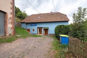A two-story building with a blue facade, a tiled roof, and a gravel driveway leading to a wooden gate.