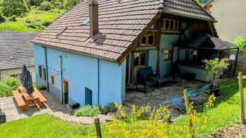 Un chalet tradicional con techo inclinado, un patio con mobiliario exterior y vistas a un paisaje verde exuberante.