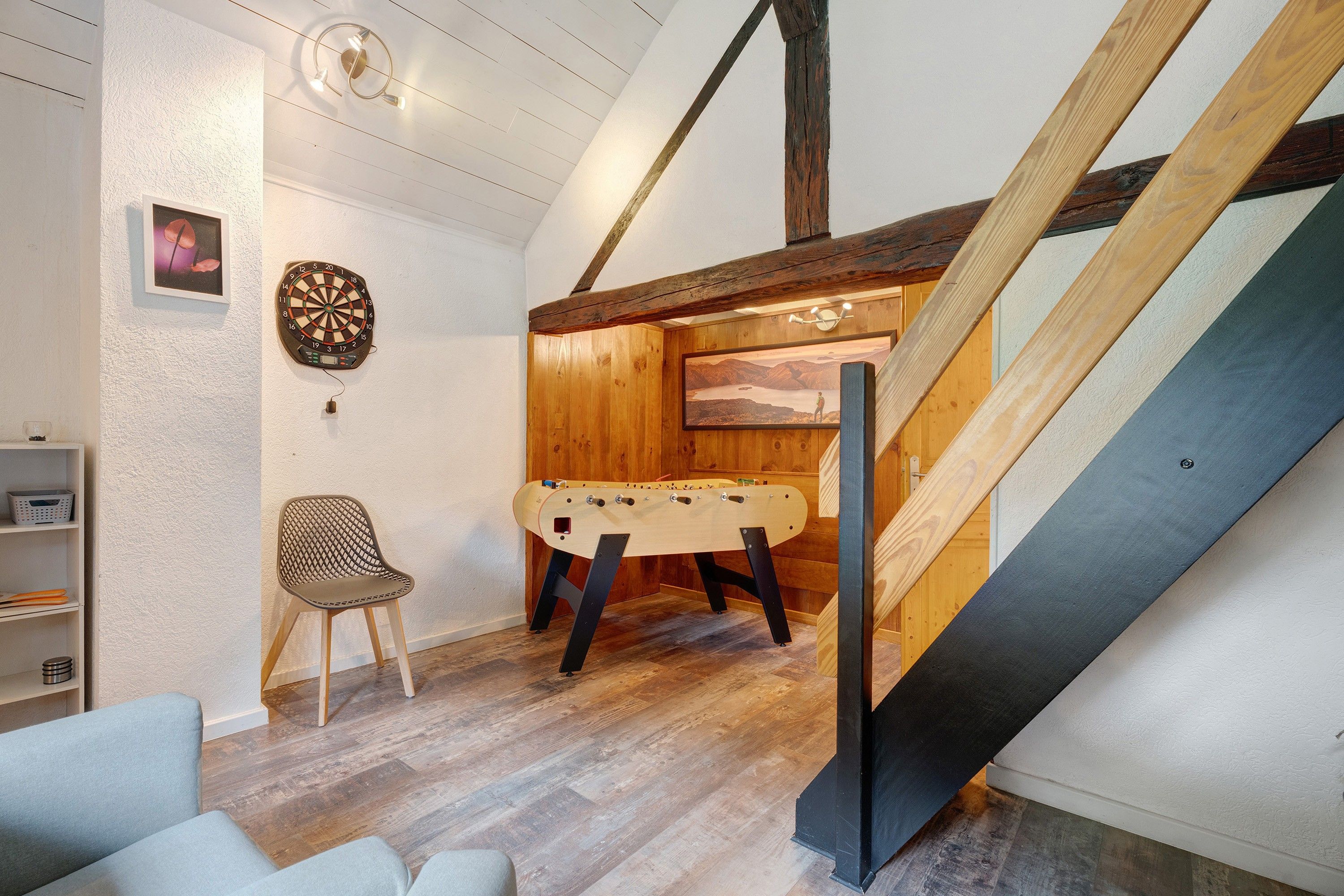 Ein gemütliches Zimmer mit einem Kicker, einer Dartscheibe und einer Holztreppe.