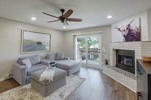 A modern living room with a sectional sofa, a fireplace, and a large window. - Tasteful Townhome Near Black Hills National Forest (Rapid City)