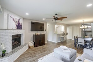 A modern living room with a fireplace, a flat-screen TV, and a dining area with a chandelier. - Tasteful Townhome Near Black Hills National Forest (Rapid City)