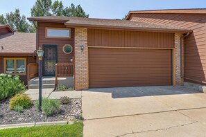 A residential garage with a brown exterior, a brick accent wall, and a metal garage door. - Tasteful Townhome Near Black Hills National Forest (Rapid City)