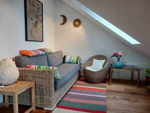 Ein gemütliches Wohnzimmer mit grauem Sofa, Korbstühlen, einem Streifen Teppich und einem Oberlicht.