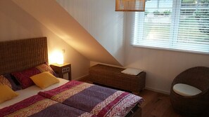 Ein Schlafzimmer mit Bett, Nachttisch, Lampe und einem Korbsessel.