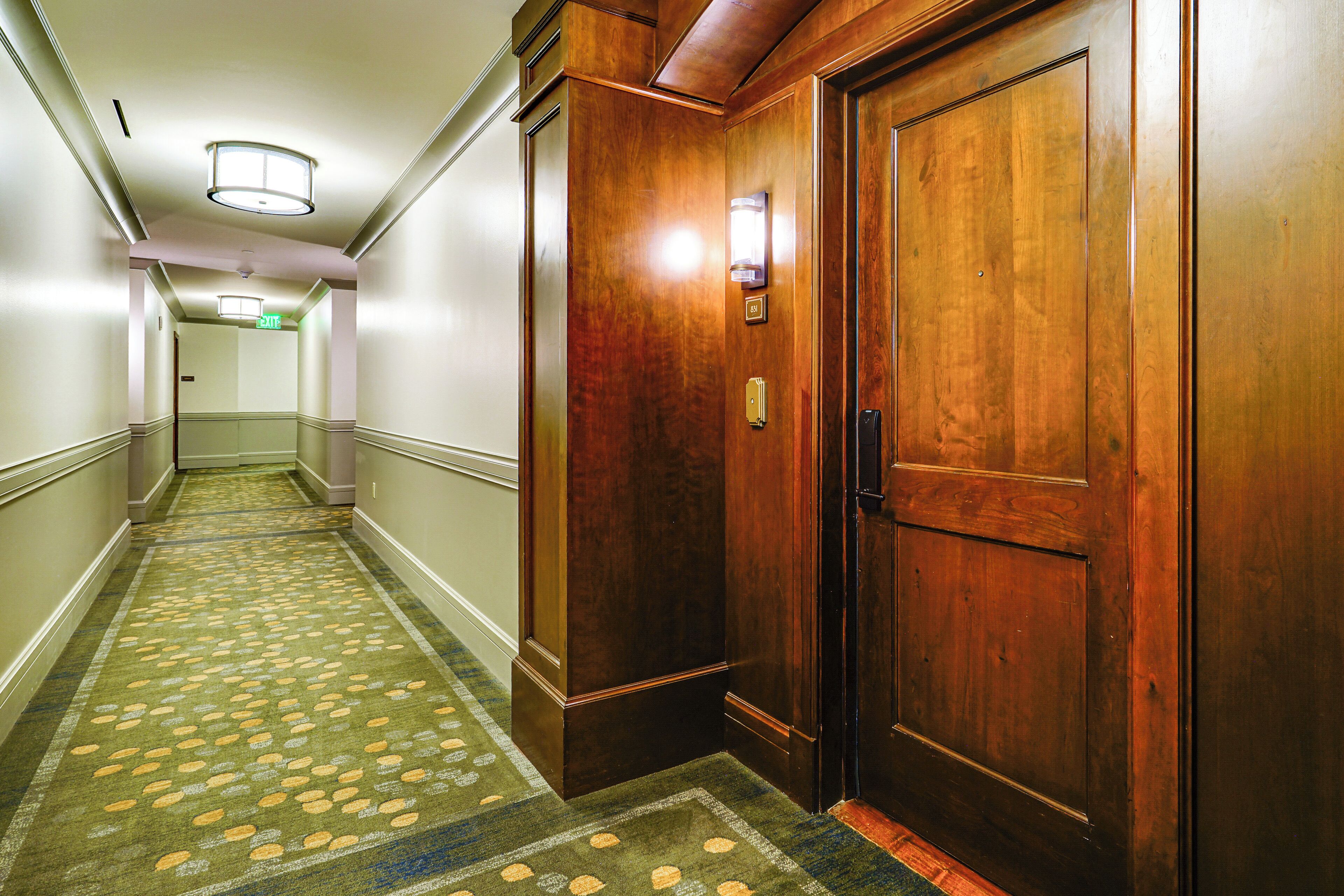 Un pasillo de hotel con piso alfombrado, puertas de madera y una lámpara en el techo.