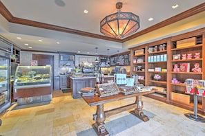 A café interior with a central island, a cash register, a menu board, and shelves stocked with snacks and beverages. - Ski-In/Ski-Out! Mtn-View Montage Deer Valley Condo (Park City)