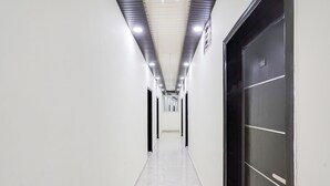 Un pasillo con paredes blancas, suelo de mármol y una puerta de ascensor negra con placa numérica.