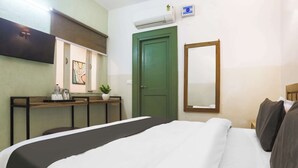 Habitación de hotel con cama, escritorio con computadora, puerta verde y equipo de aire acondicionado.