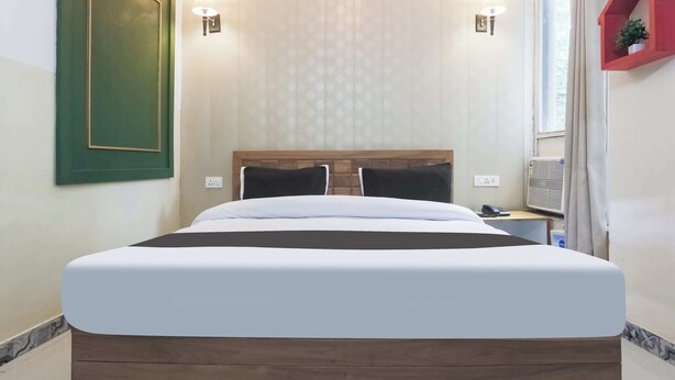 Habitación de hotel con una cama grande, dos lámparas de noche, un estante para plantas rojo y una ventana con cortinas.
