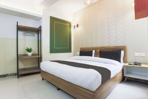 Hotellihuone, jossa on sänky, yöpöytä, lamppu ja seinälle ripustettava naulakko.