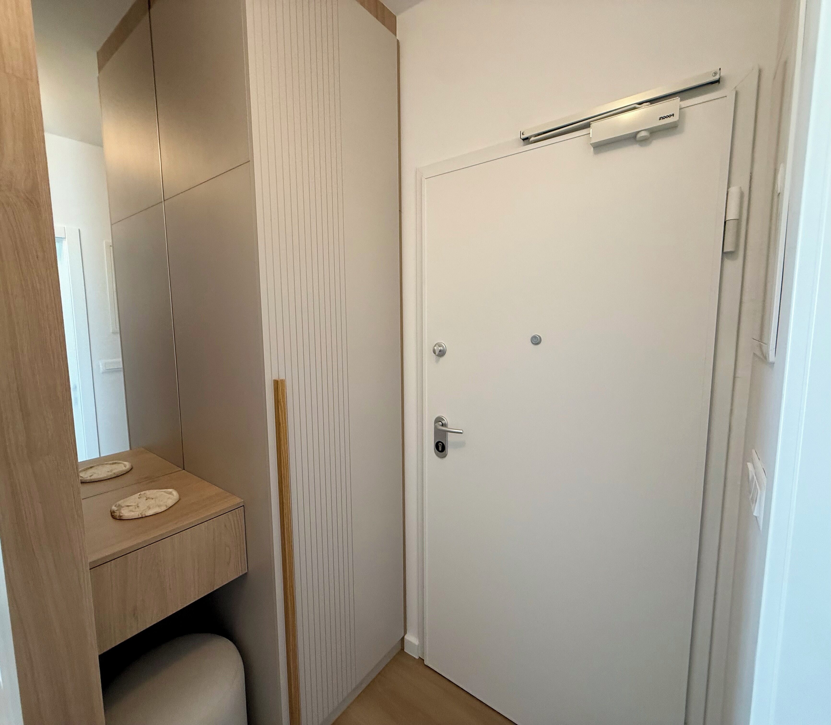 A white door with a handle and a lock, a small wooden bench with two flat objects on it, and a vertical wooden panel with a geometric pattern.