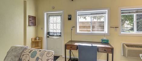 A room with a sofa, a desk, a chair, a door, and windows.