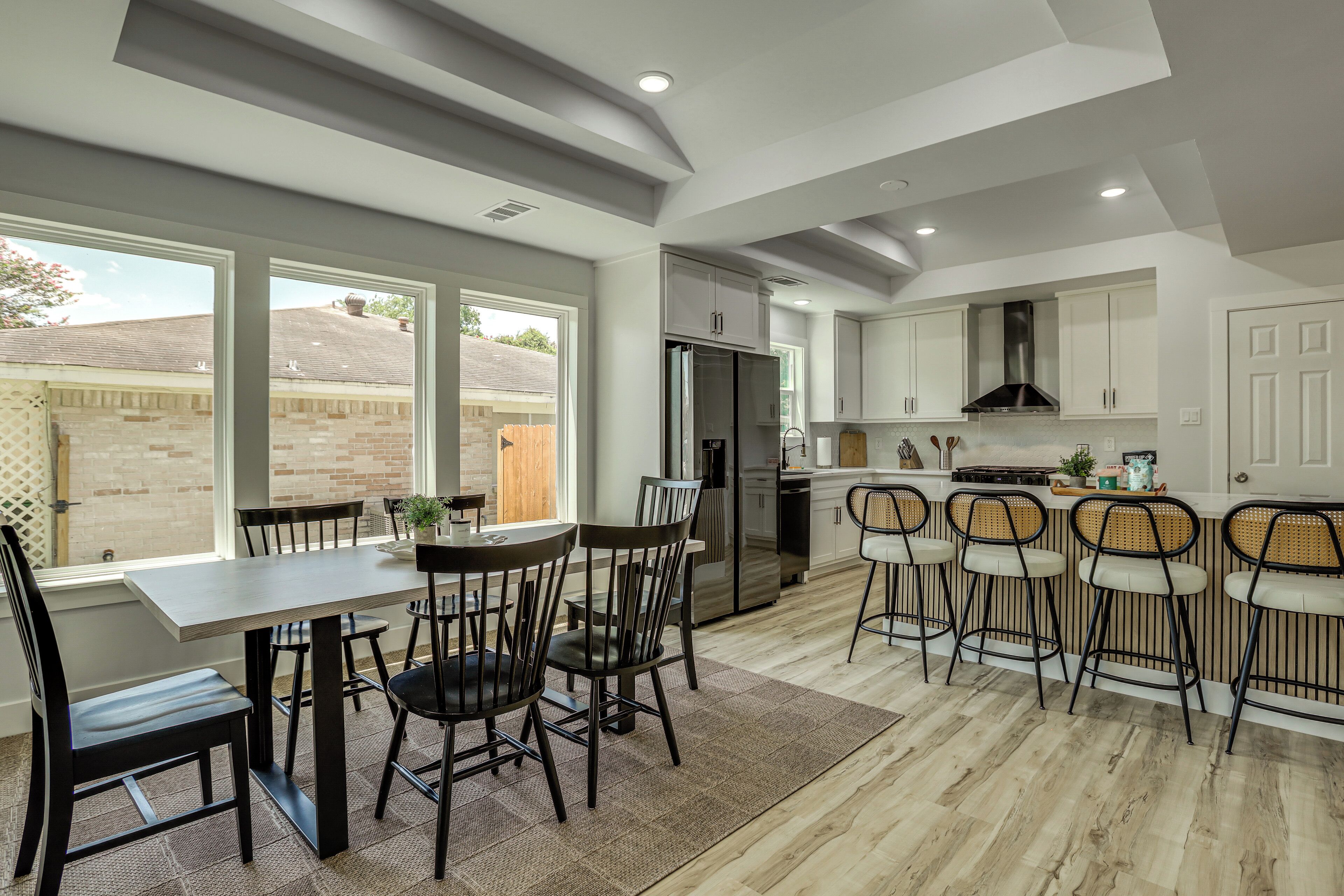 A modern kitchen with a dining area, large windows, and a view of the backyard.