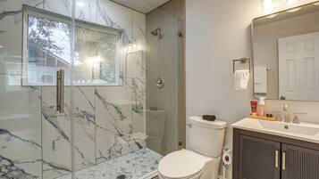 A bathroom with a glass-enclosed shower, a toilet, a sink with toiletries, and a mirror.