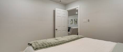 A bedroom with a bed, a ceiling fan, a door, and a light switch.