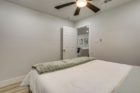 A bedroom with a bed, a ceiling fan, a door, and a light switch.