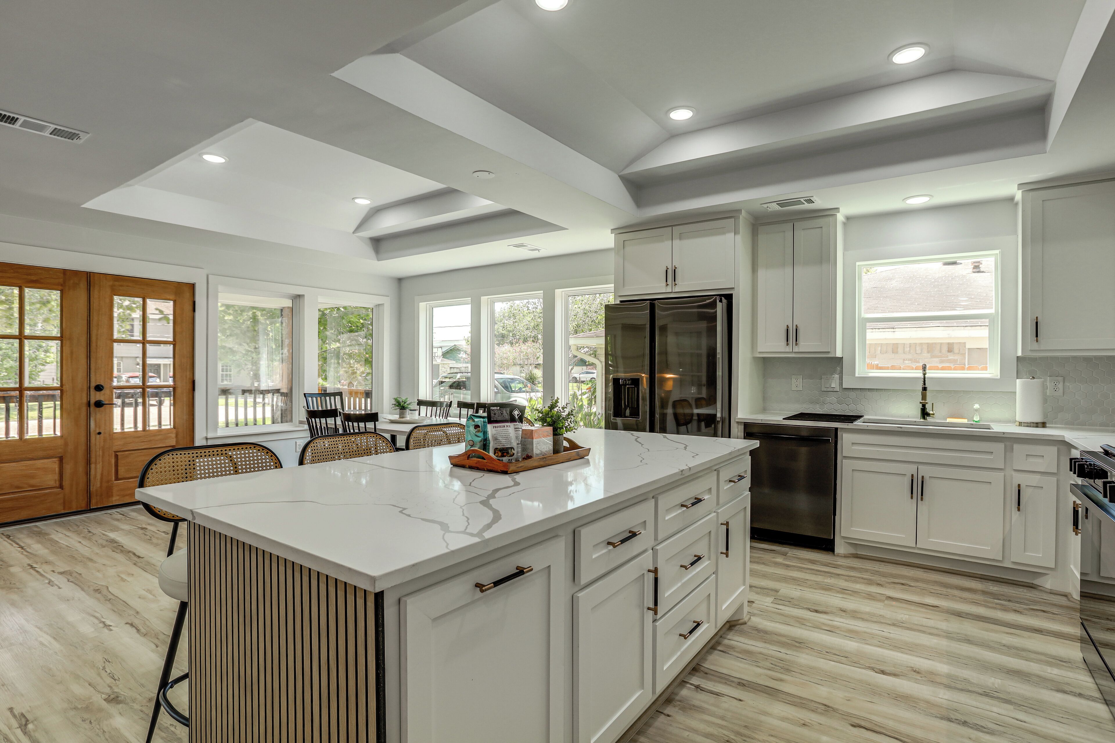 A modern kitchen with a large island, stainless steel appliances, and a view to the outside.